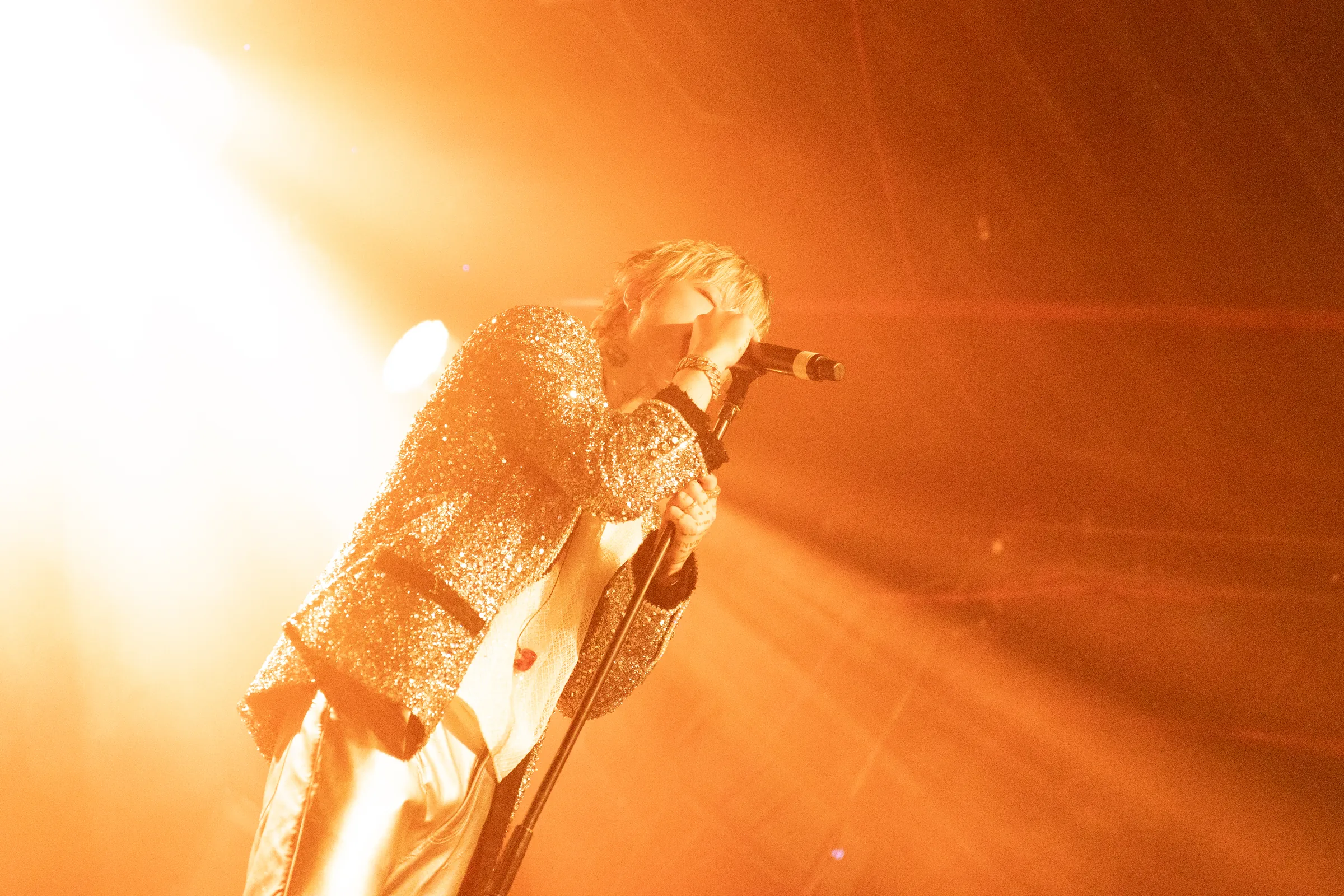 ASH ISLAND singing in a sparkling jacket under orange backlight
