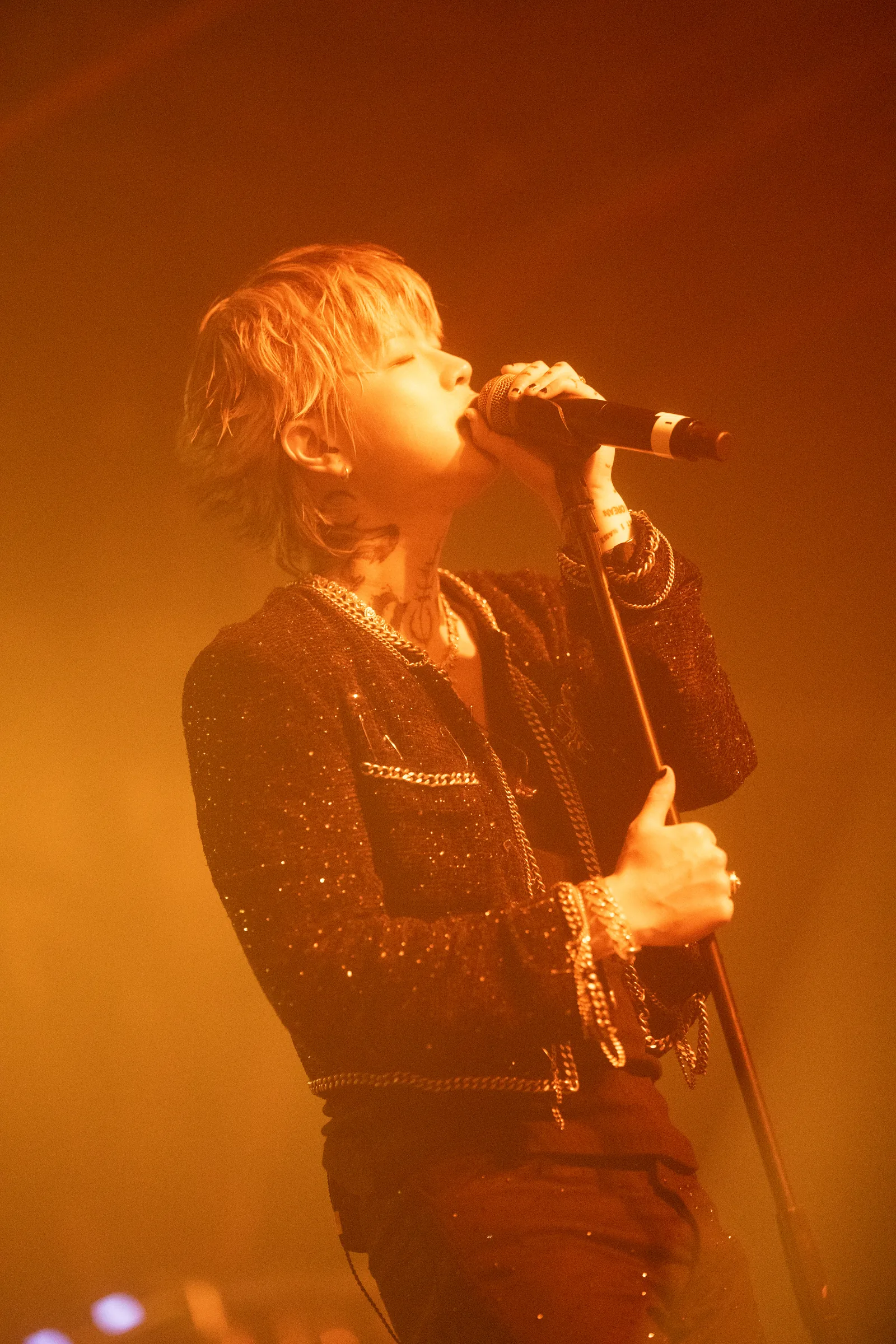 ASH ISLAND singing in a sparkling jacket under orange stage light